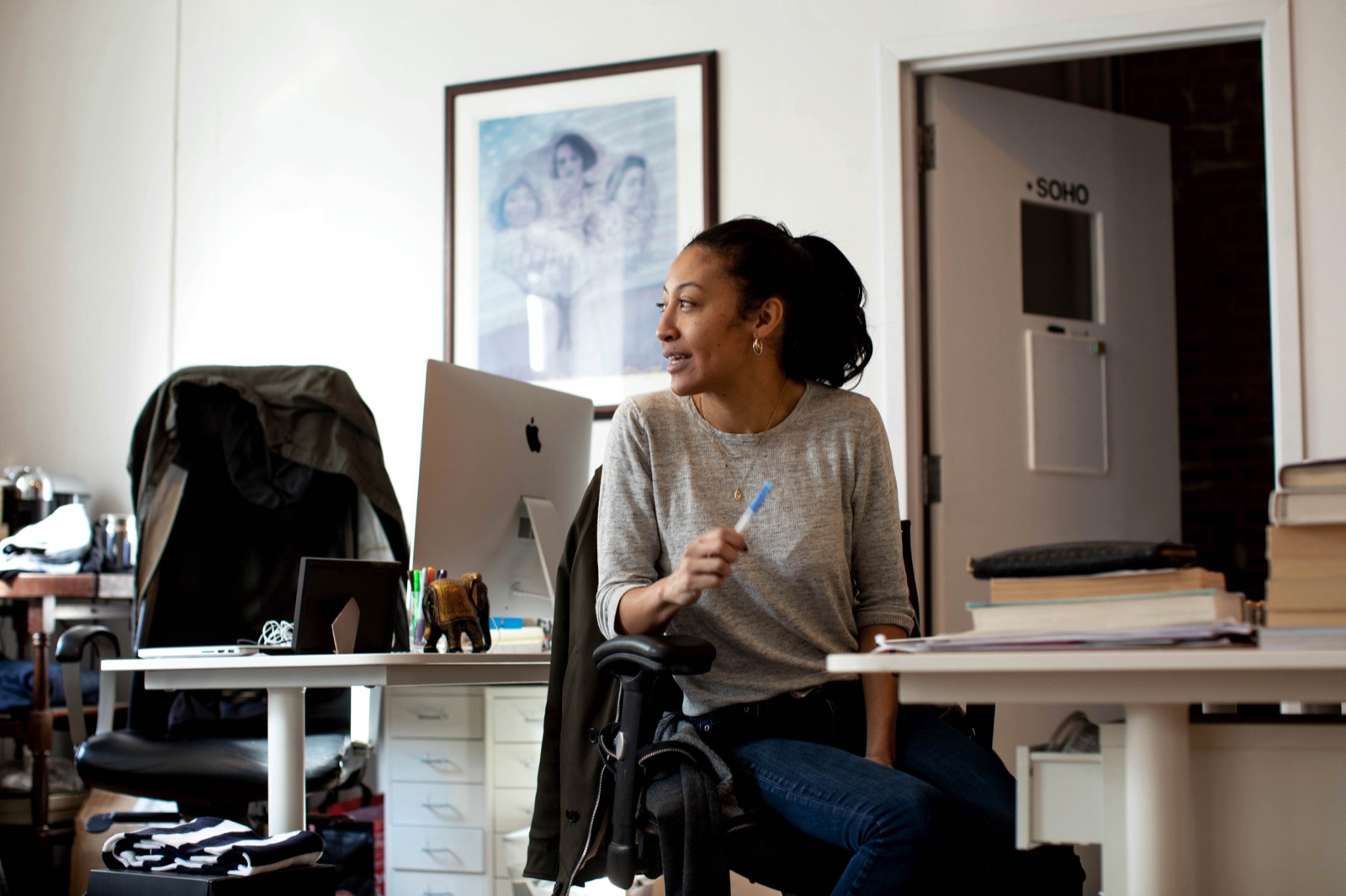 A marketer at her desk in an open-plan office, looking up from her computer.